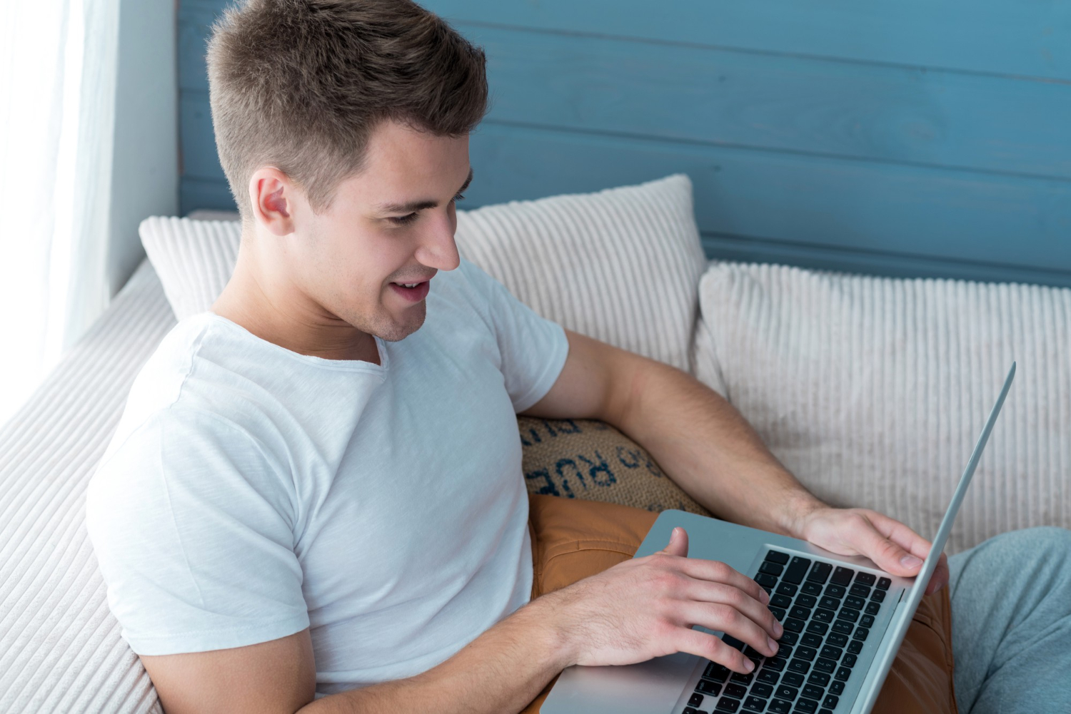 A guy is lying on the couch with a laptop in his hands