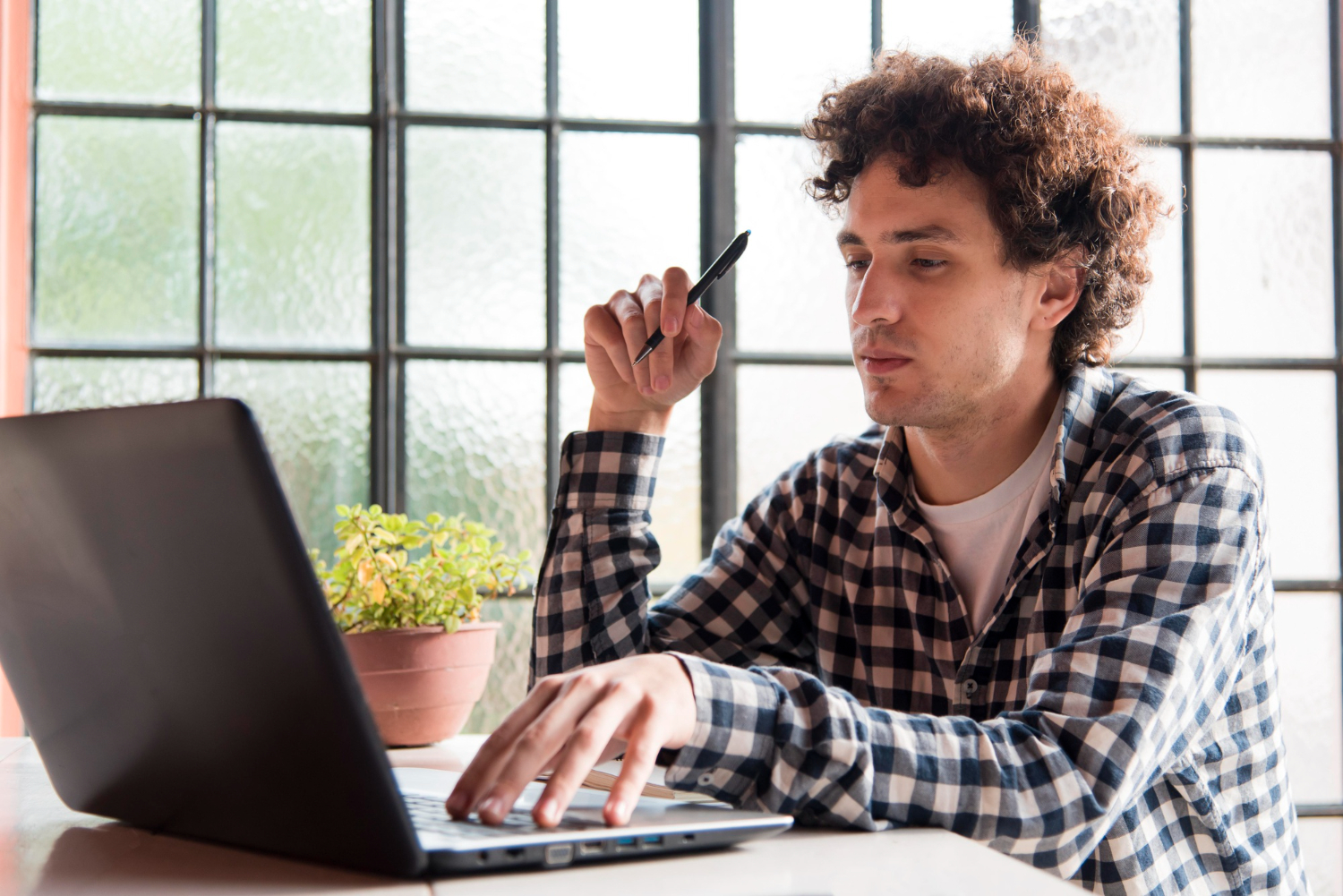 A man with a pen in his hand uses a laptop
